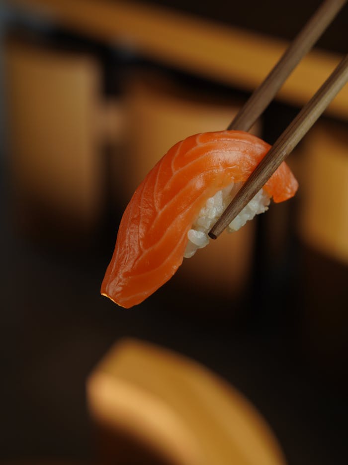 Detailed close-up of a fresh salmon sushi piece held by chopsticks, emphasizing its vibrant texture and color.